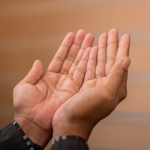 Two open, upturned hands held together in a gesture of offering and receiving, against a soft warm background