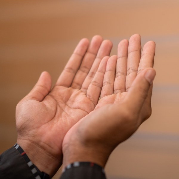 dana-gratitude-square-product Two open, upturned hands held together in a gesture of offering and receiving, against a soft warm background