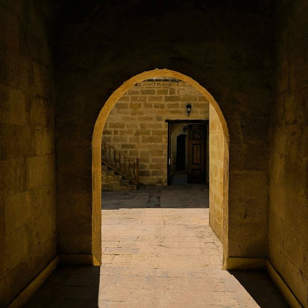 Warm sunlight spilling through an old stone archway onto a worn stone floor, opening toward a quiet courtyard and stairway beyond